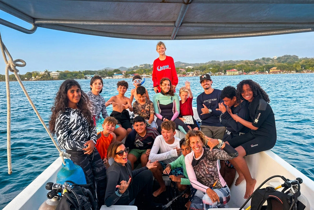 A group of people posing together on a boat on the water, wearing various casual and wetsuit outfits under a canopy. Dive scouts students